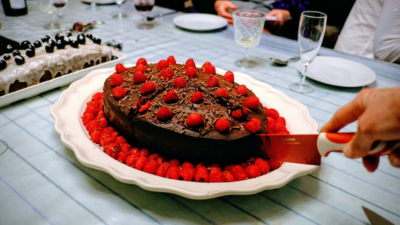 a hand cutting an oval chocolate raspberry cake