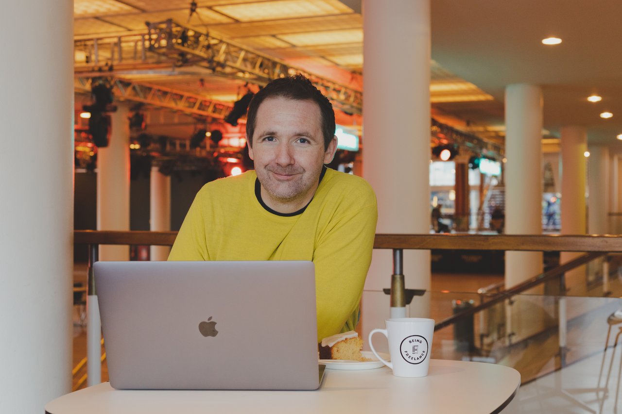 Steve wearing a yellow jumper with his laptop and mug of tea