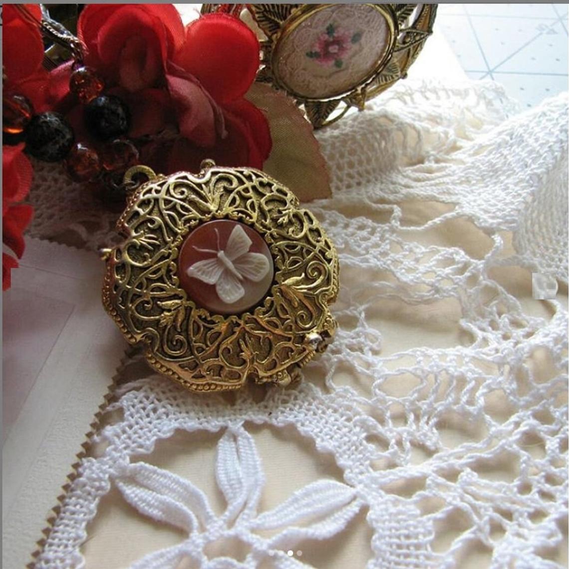 A picture of a vintage butterfly locket surrounded with lace and faux roses