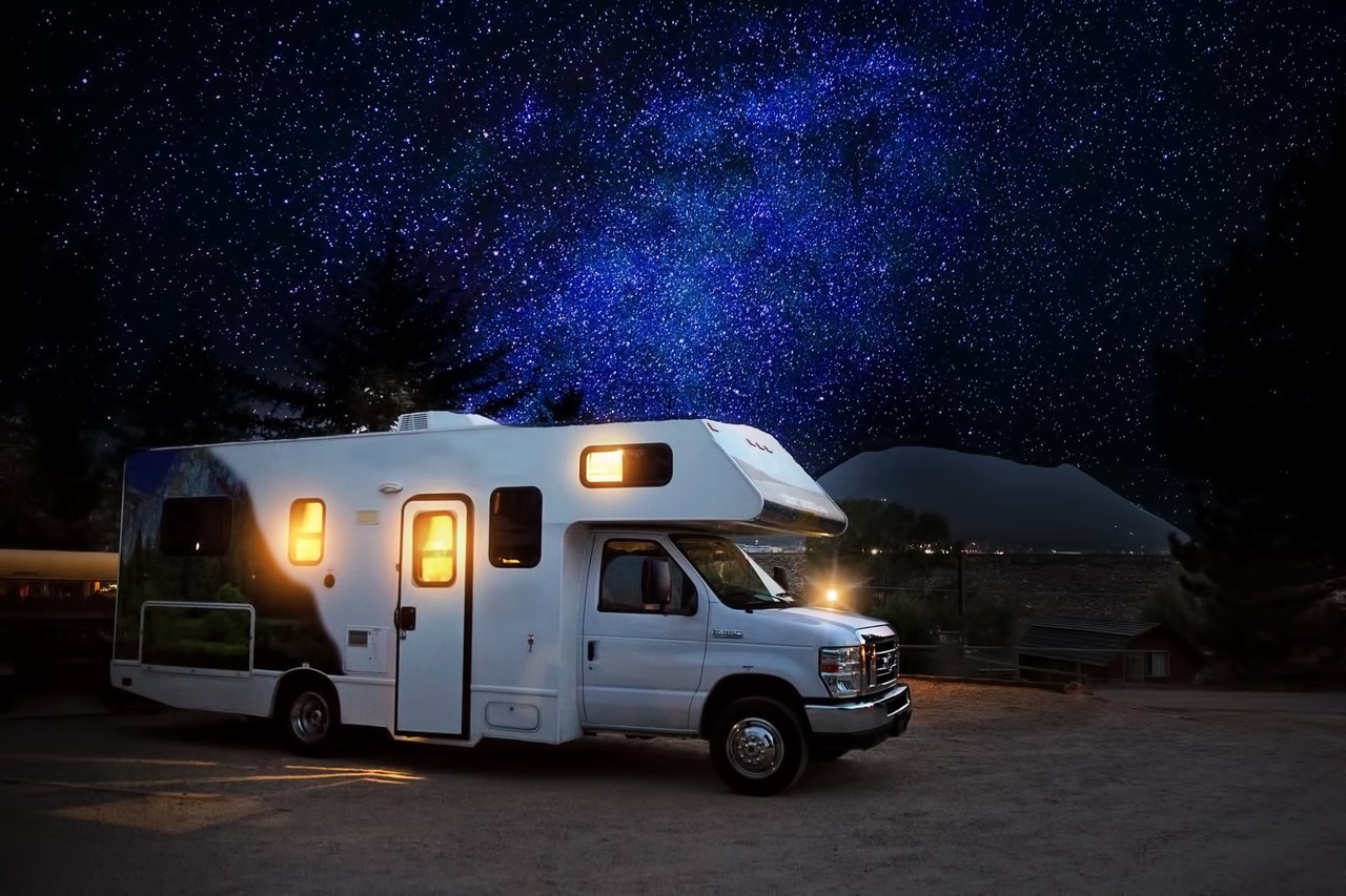 A Class C Motor Home parked under a starry sky has lights and power from an onboard motorhome generator