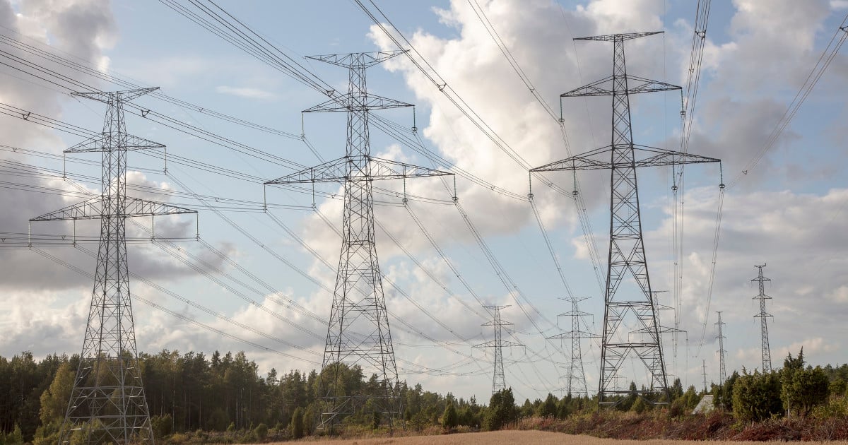 Steel Transmission Towers Support Multiple Long Distance Transmissions Lines against a blue sky with clouds. The right-of-way through a forest is clear of trees.
