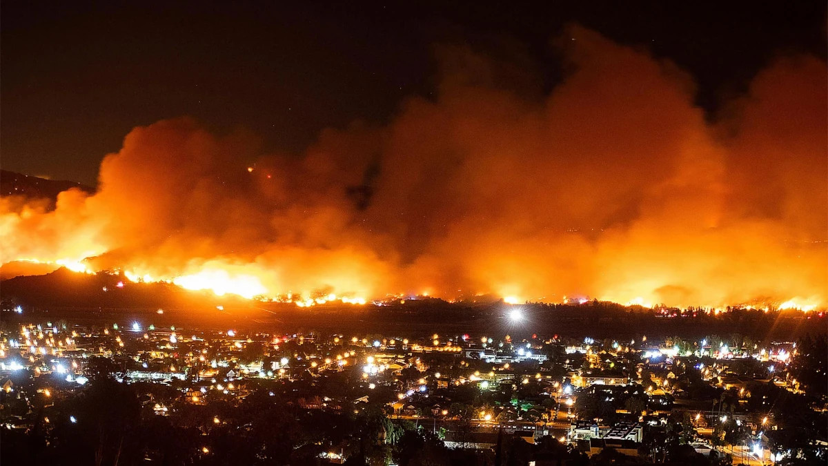 A Wildfire raging out of control in California approaches a community, forcing evacuations and burning homes.
