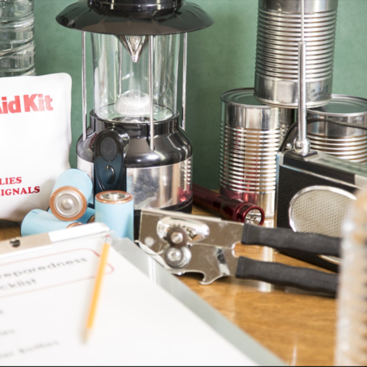 Hurricane Preparedness Supplies with a checklist on a clipboard. Pictured is a partial list of supplies including canned food and a can opener, gas lantern, batteries, first aid kit, radio, and a water bottle