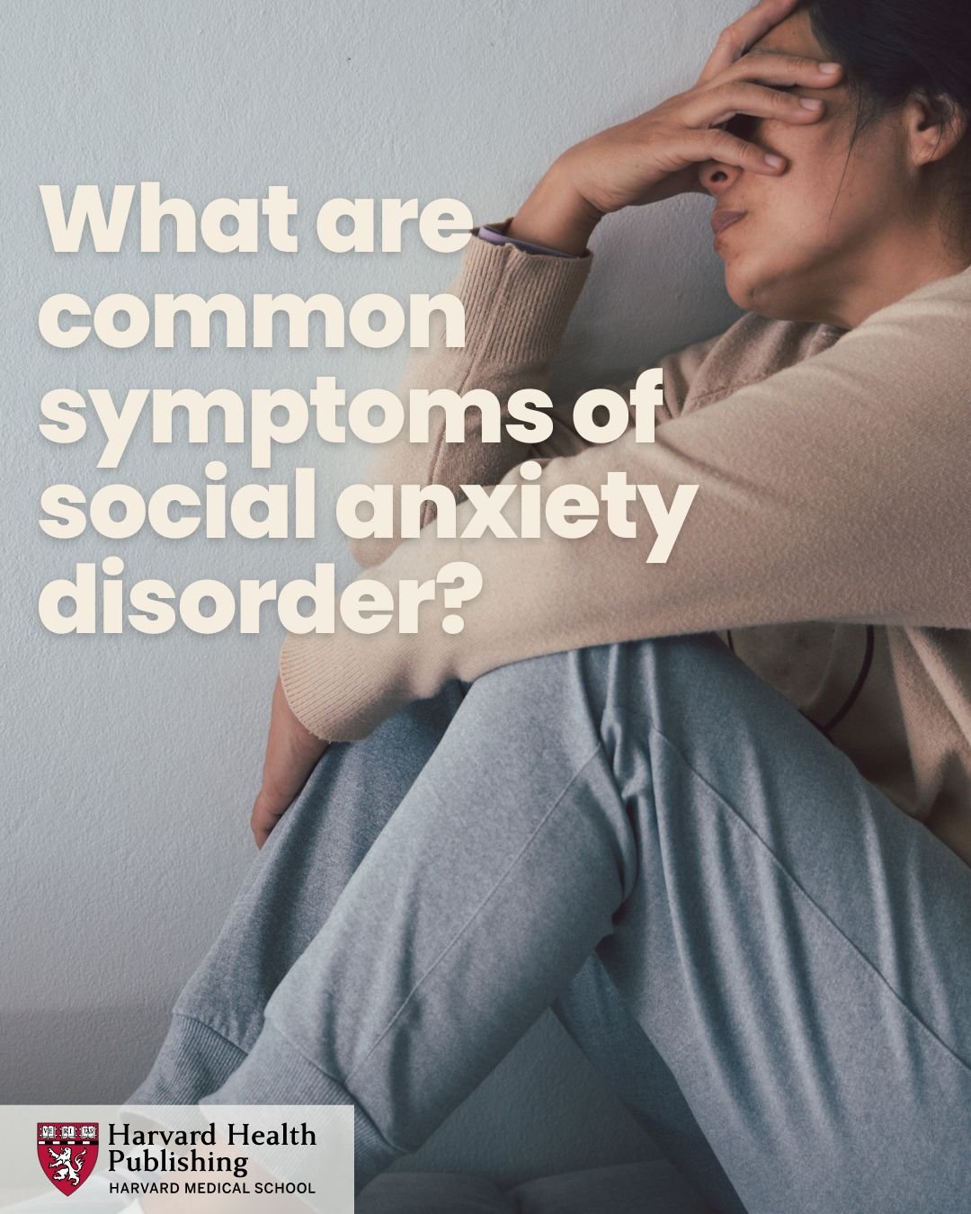 young woman sitting against a wall with her head in her hands.