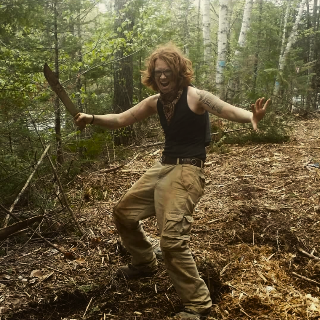 V brandishing a brush machete in the woods