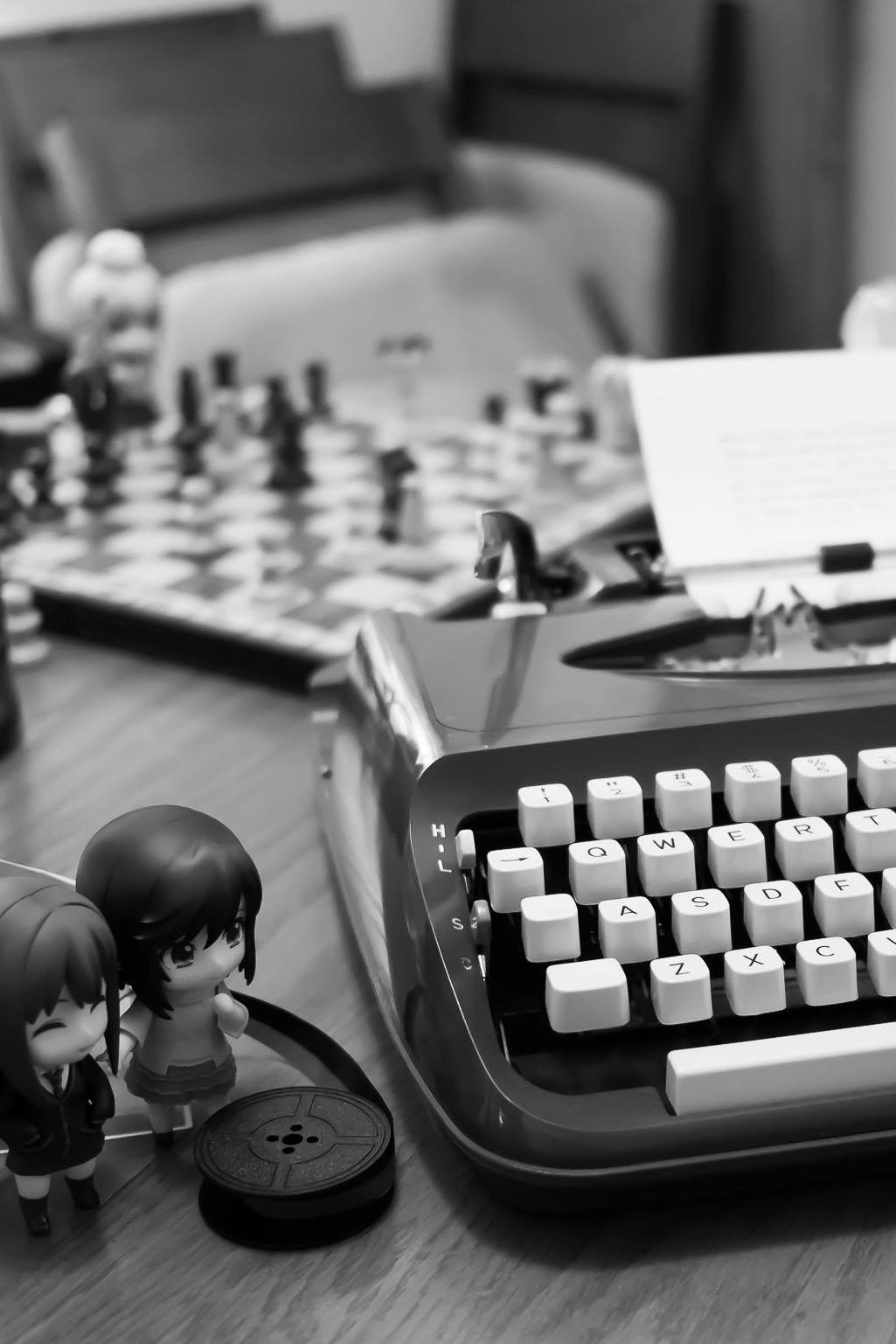 Black and white photograph of manual typewriter with figurines standing beside it.