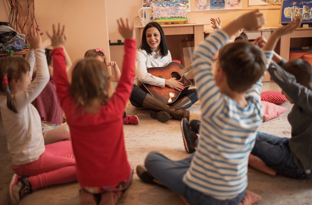 woman playing guitar and preschoolers have their hands up