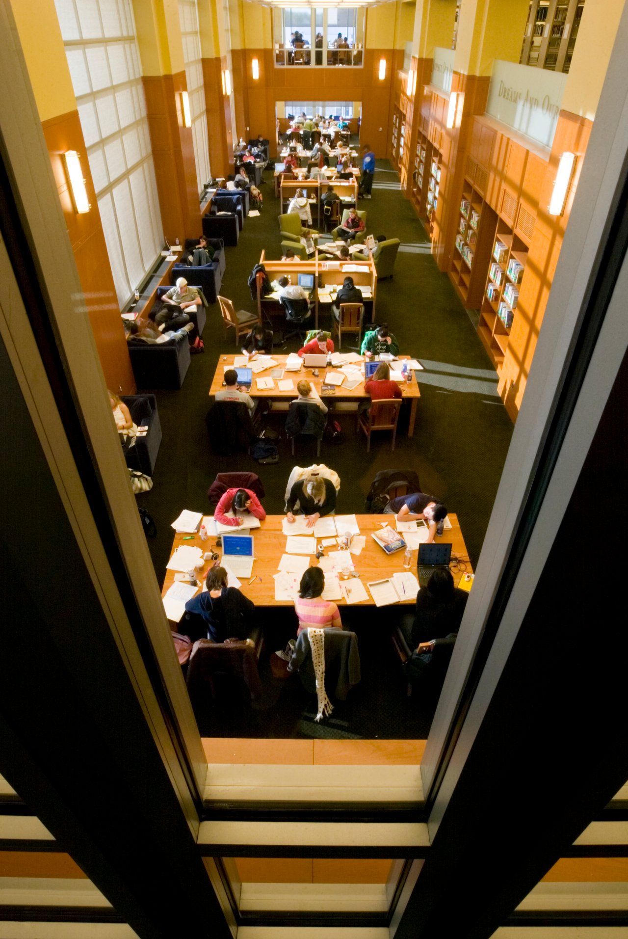 Students sit at tables strewn with papers and laptops in a section of Bostock library