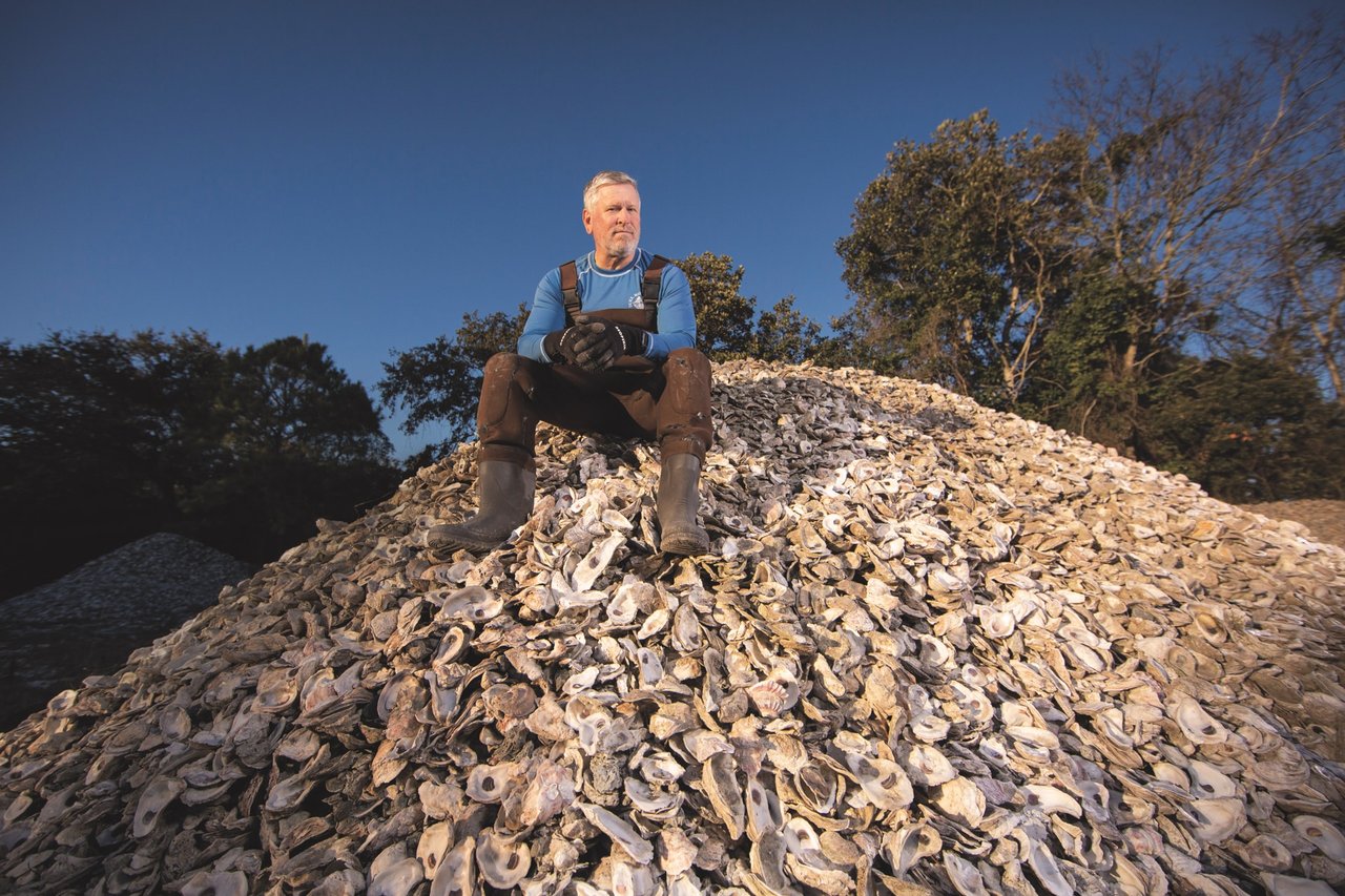 A person sits on top of a giant pile of oyster shells