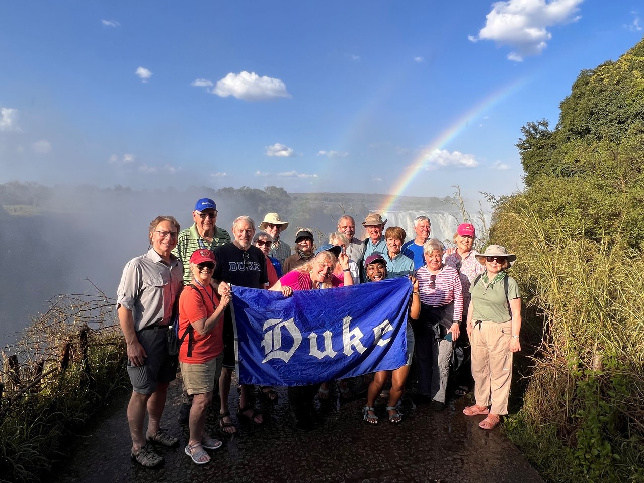 People standing in front of Victoria Falls holding a Duke flag
