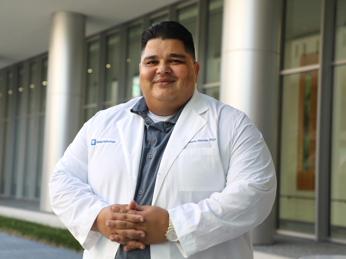 Everardo Macias wears a white coat and stands outside a building.