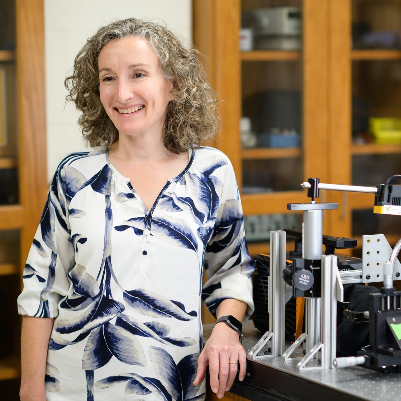 Duke Professor Shelia Patek smiling and looking off-center, leaning against a table with microscope in the background.