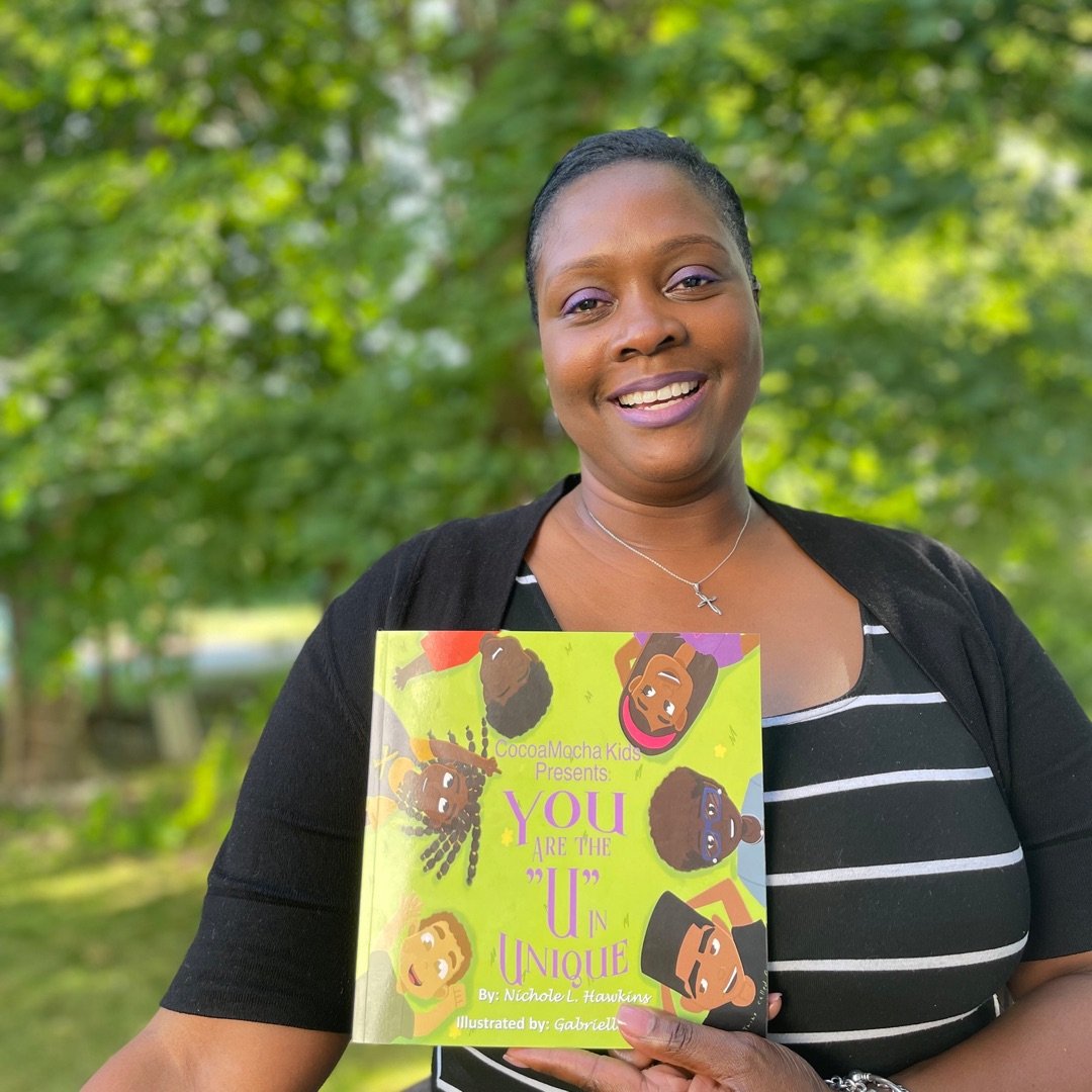Beautiful black woman smiling holding a book that has an  Illustration of 6 beautiful black children smiling.