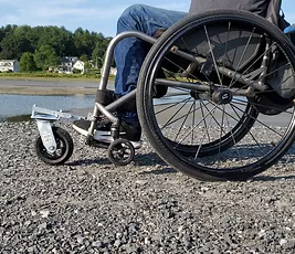 A wheelchair with a single larger wheel in the front moving on gravel.