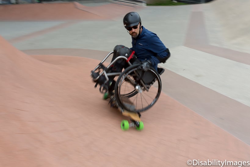 Wheelchair user on an electric skateboard in a skateboard park.