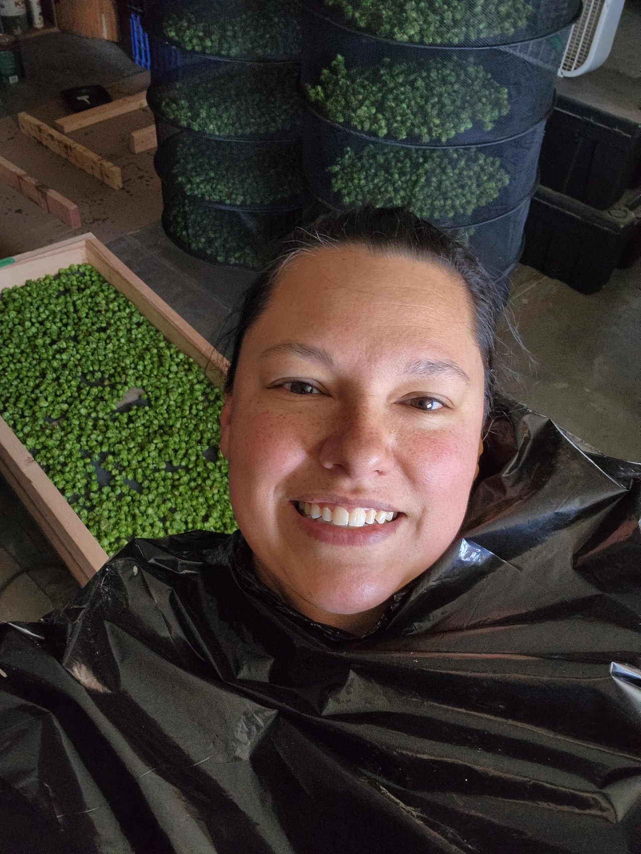 a woman taking a selfie with hops drying in the background
