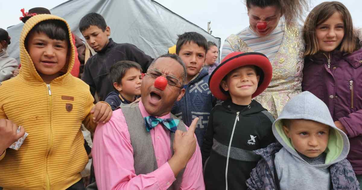Clown with a group of kids points to one child wearing a red clown hat