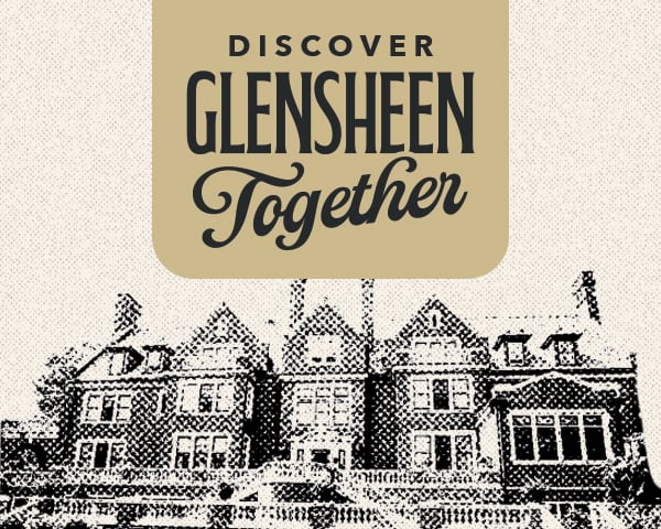 A fountain spills water over the edge into a pool as it stands in front of a red brick mansion in the sun.