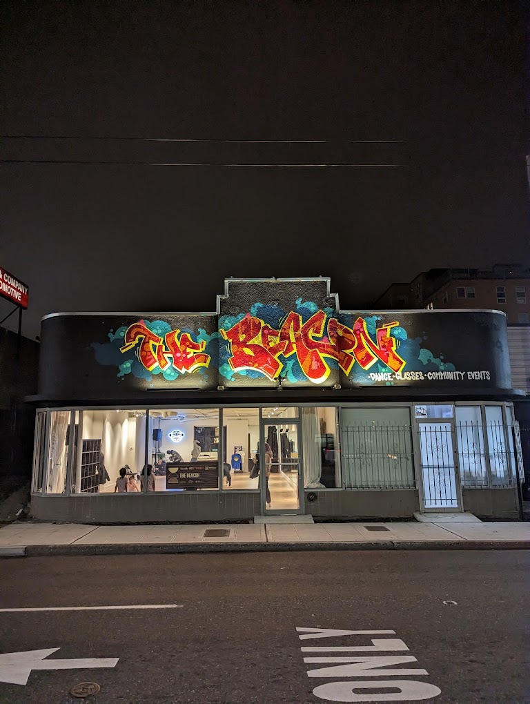 Street image of an illuminated storefront at night. Above the doors and windows is large graffiti-style text reading "The Beacon"
