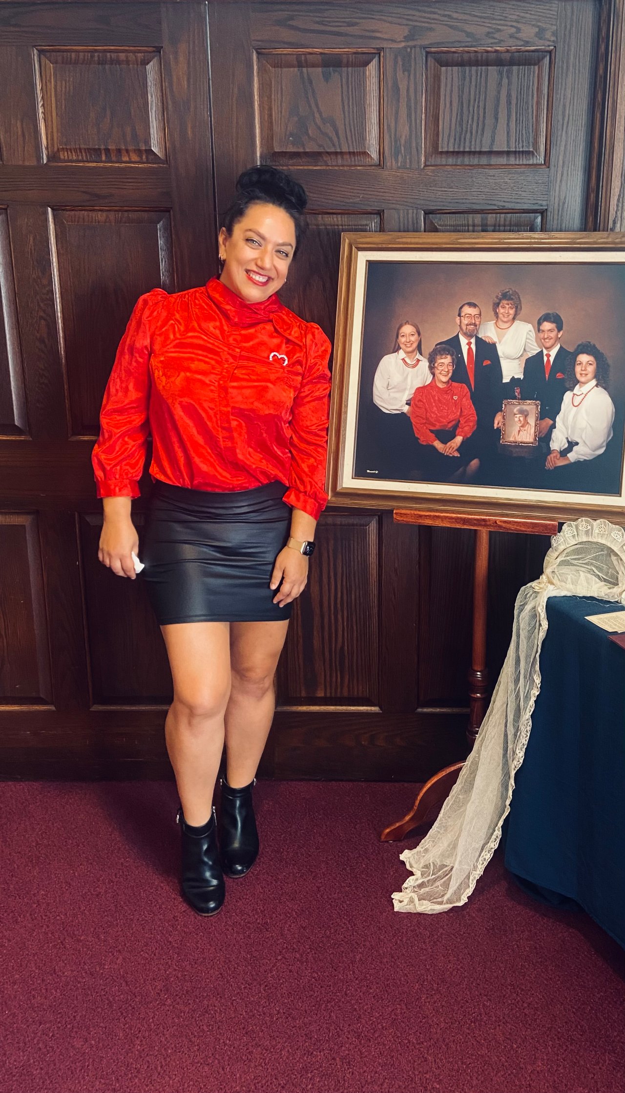 Woman at a funeral home in red standing my a family portrait.
