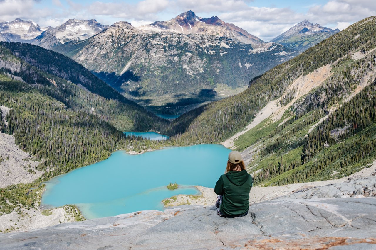 Shannon sitting at the top of a mountain, with three emerald blue lakes in the background.