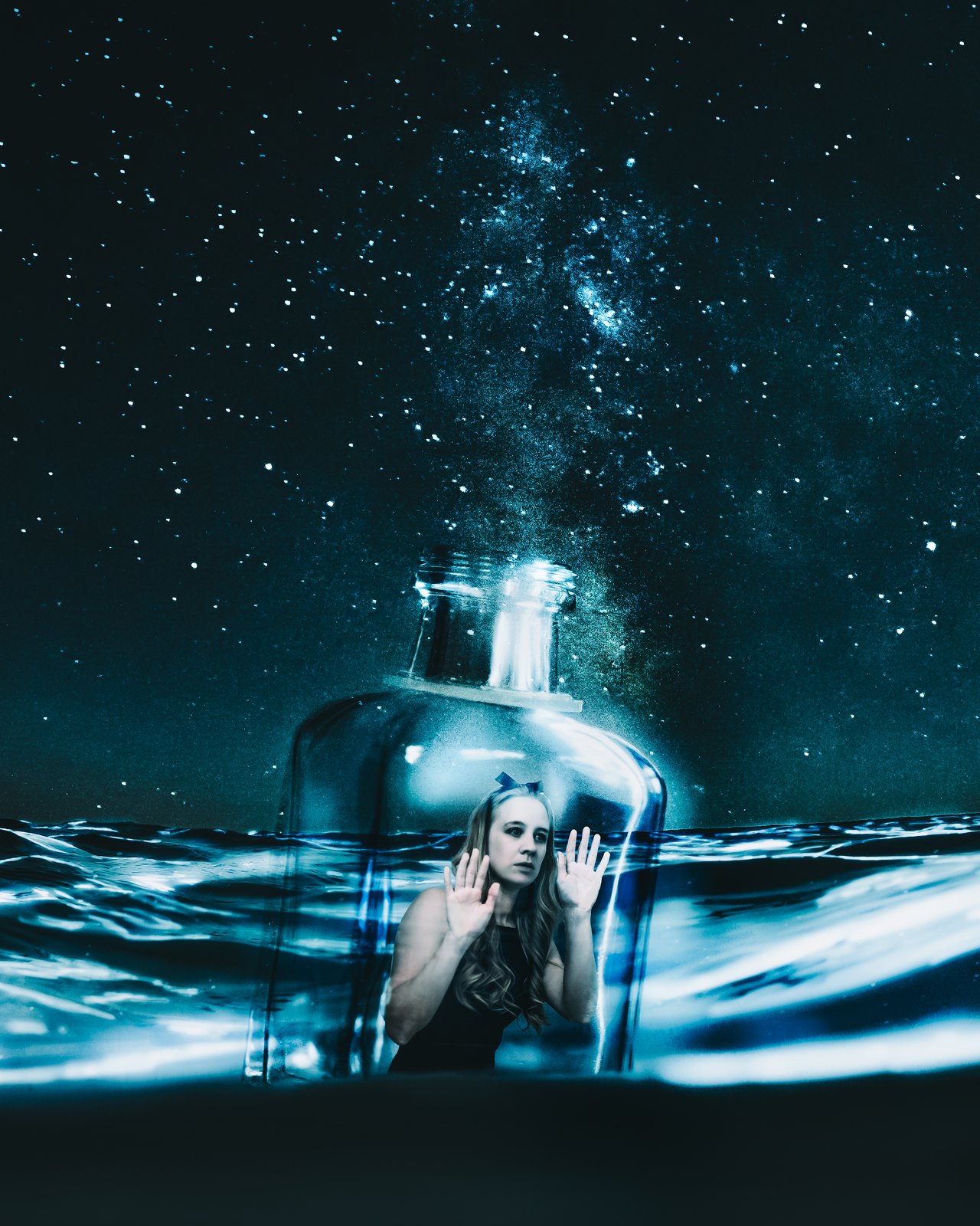 Shannon dressed as Alice in Wonderland, trapped in a bottle floating on the ocean, with the milky way in the background