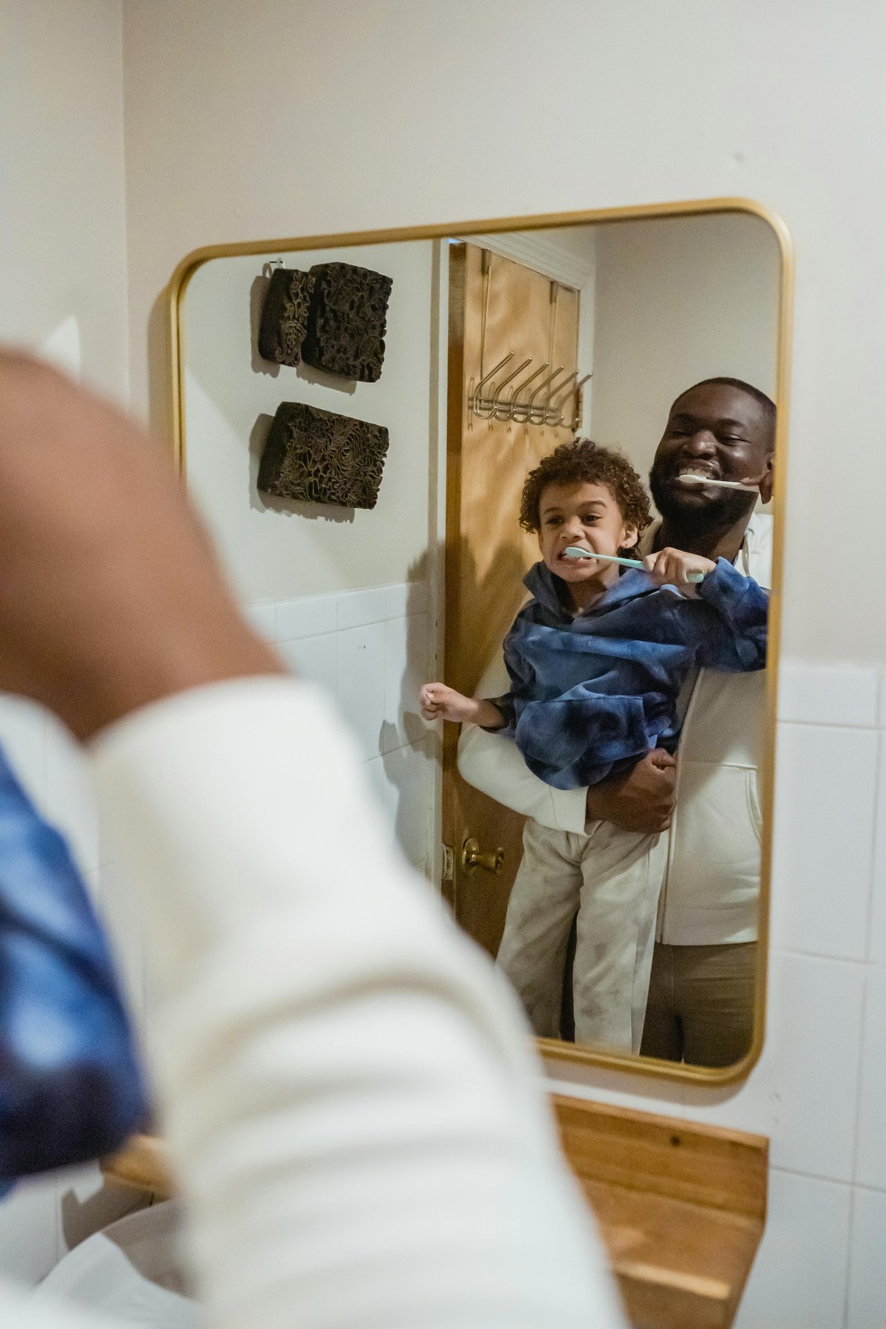 A man holding a little boy while both are brushing their teeth