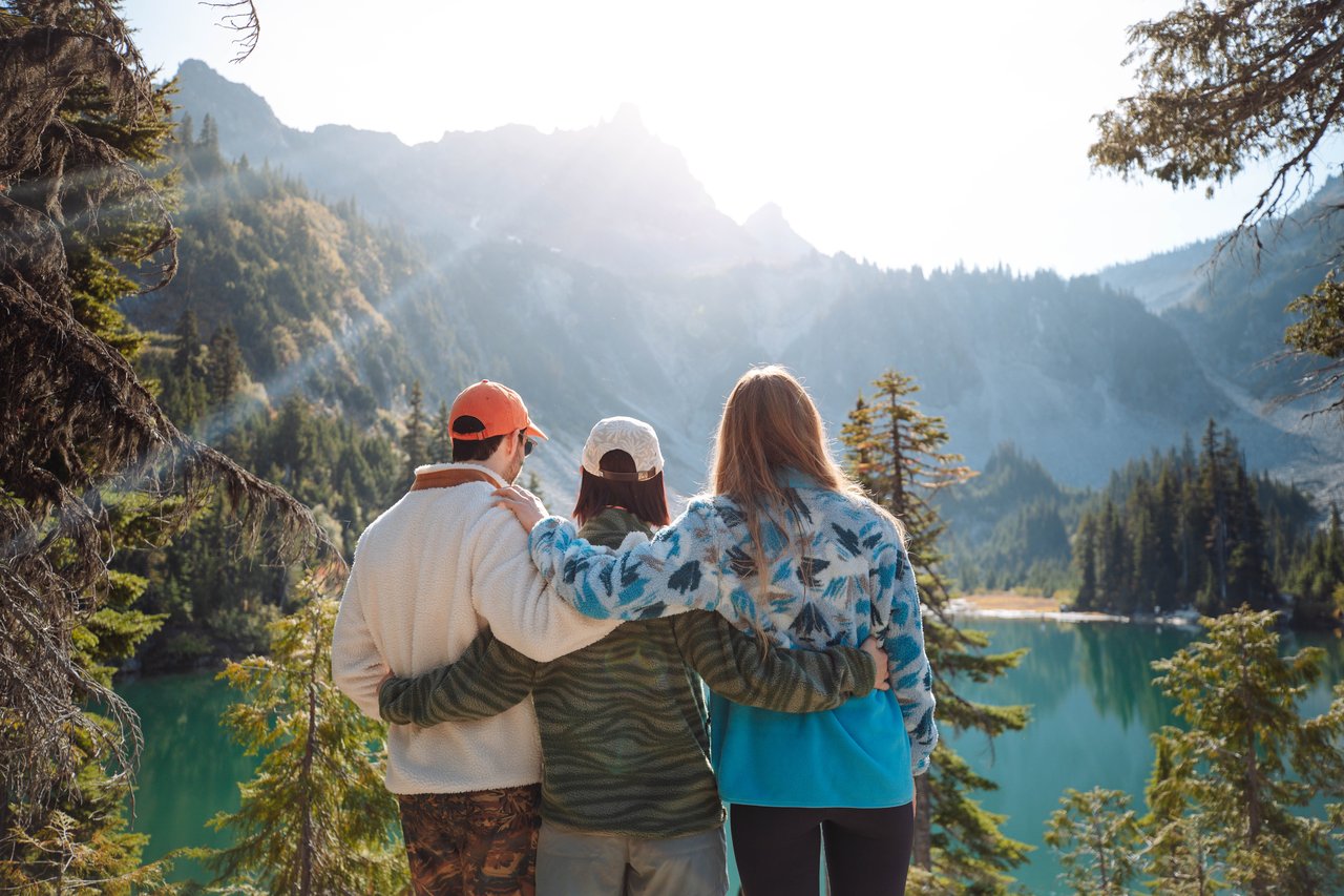 3 people with their arms around each other looking out on a lake.