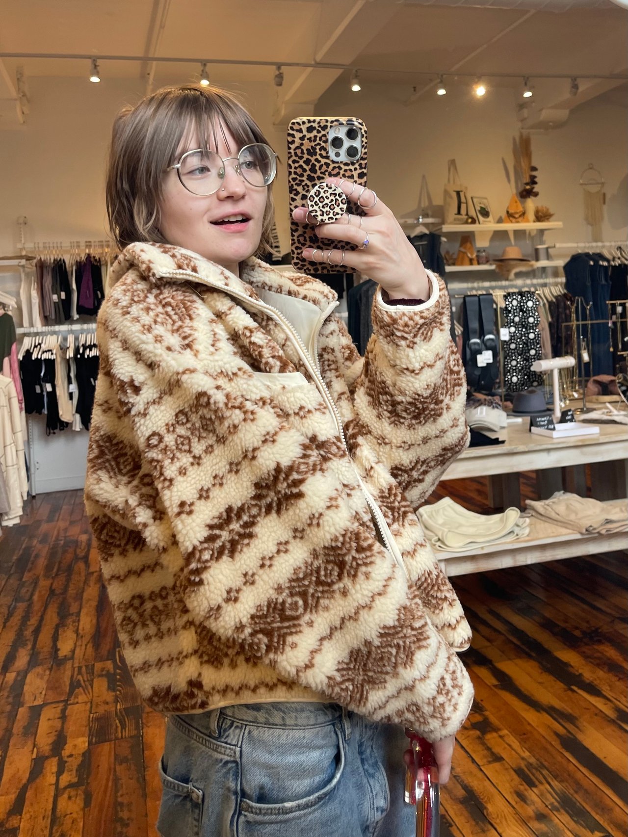Sarah taking a photo in a mirror, a slight smile smirk to her face and wearing a fashionable sweater and jeans. She looks cool.