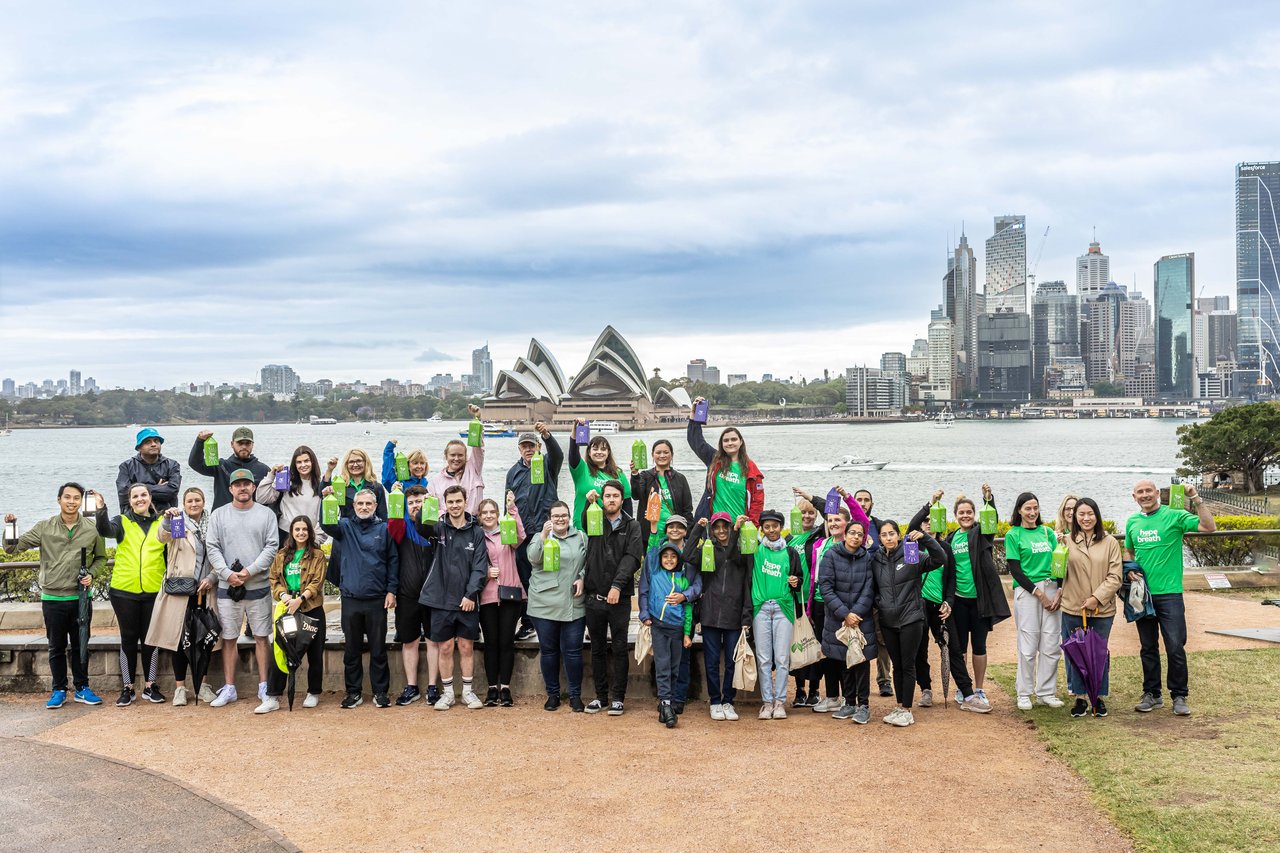A group of people holding lanterns in front of the Sydney harbour with the opera house in the background 