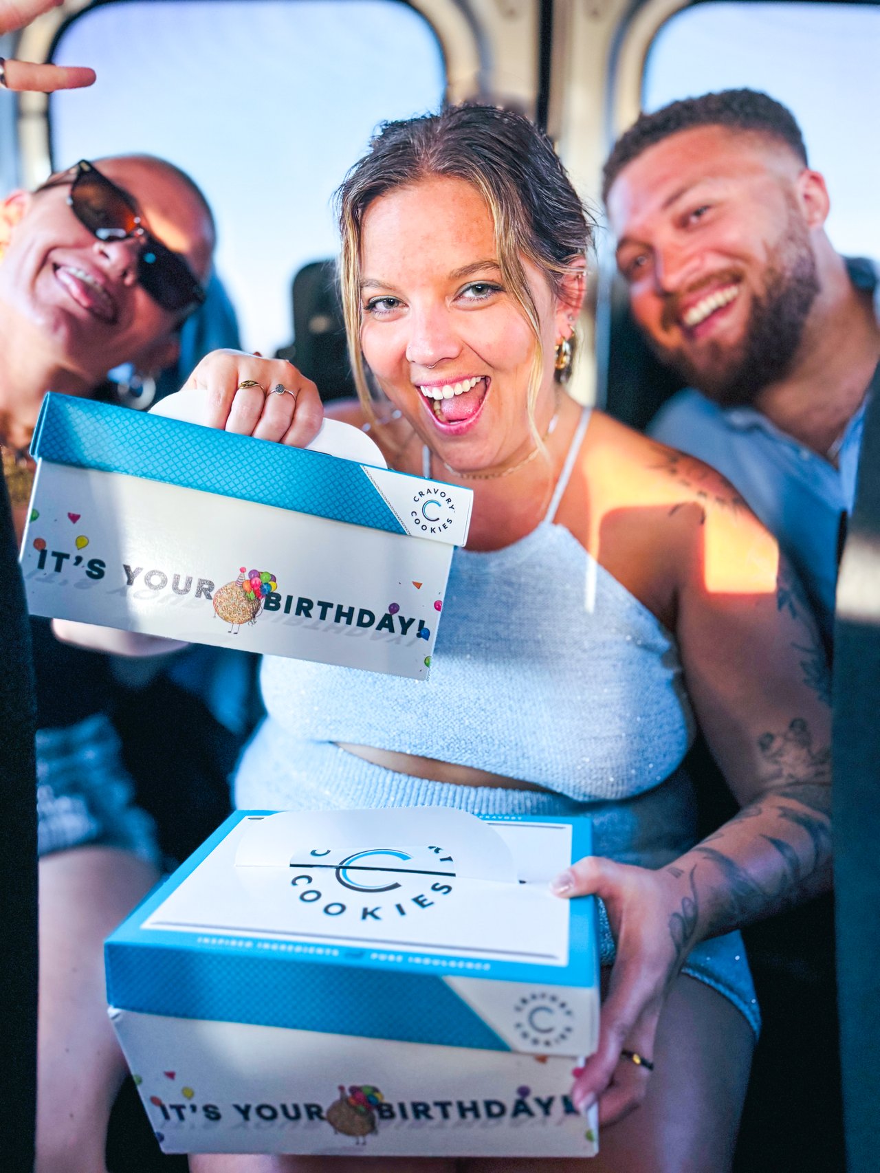 friends smiling and holding a cookie box that reads "happy birthday"