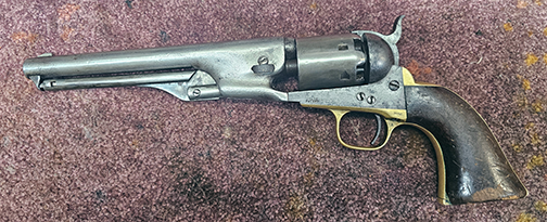 A Colt 1851 revolver, manufactured in 1861, resting on a workbench. The revolver is undergoing conservation work, showcasing its historical craftsmanship and metal details.
