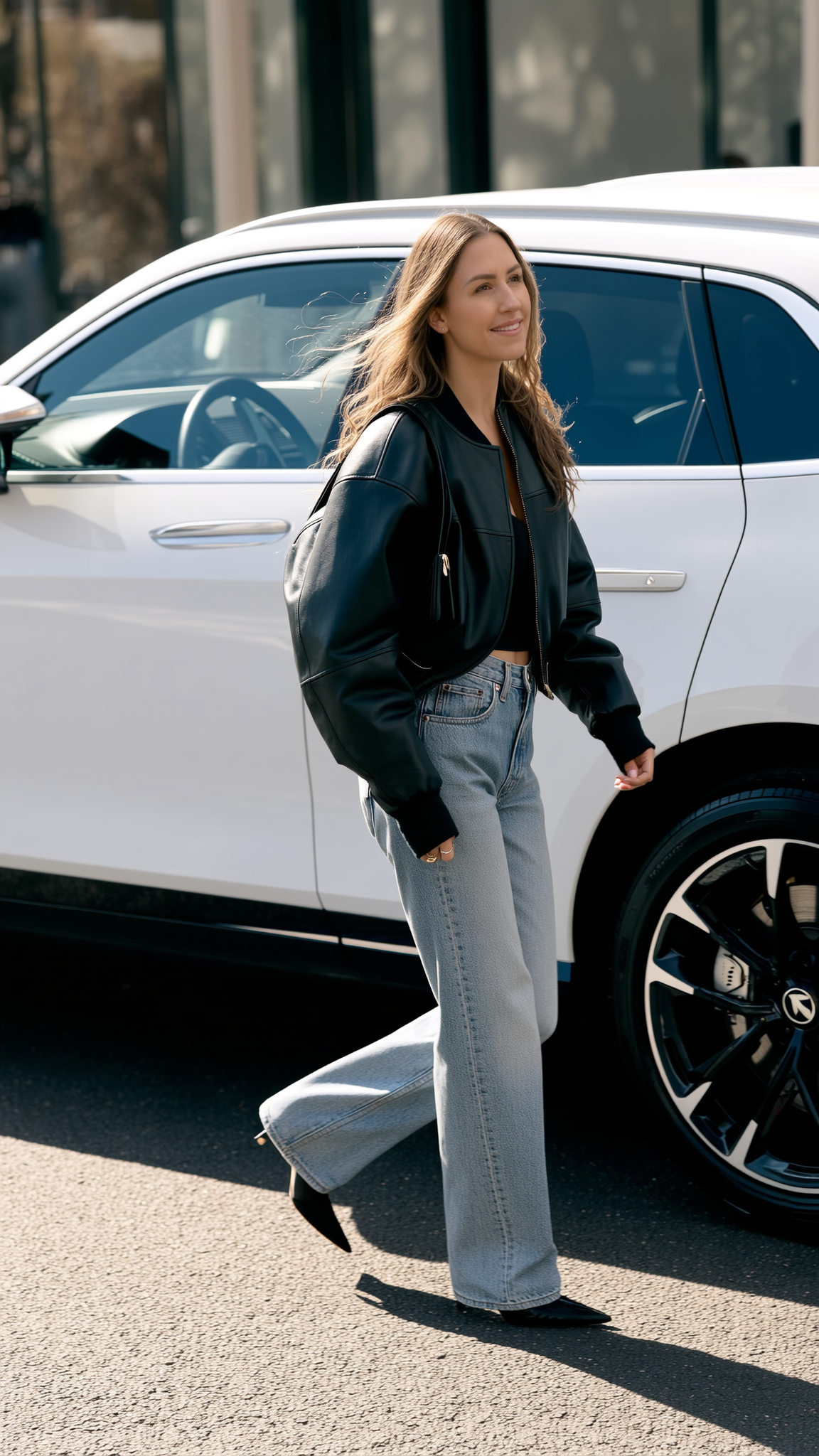 a feminine person with a full face of makeup and white leather choker and harness at a colourful rave. They're looking upwards and have a long nailed finger resting on their lips