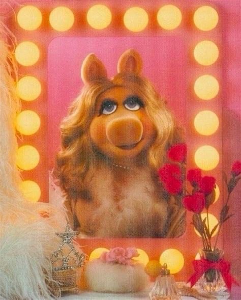 A smiling, young woman in a flower shop holding pink flowers in a vase on one hand and waving at someone off screen with the other