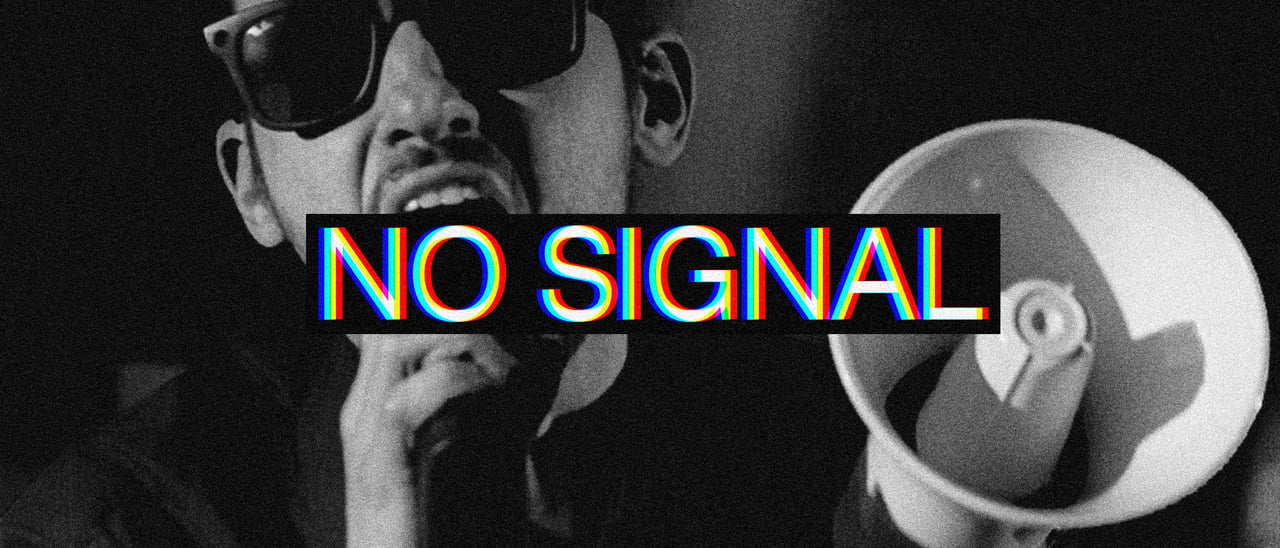 Un cantante con gli occhiali da sole che urla al microfono mentre tiene in mano un megafono. Sull'immagine c'è scritto No Signal.