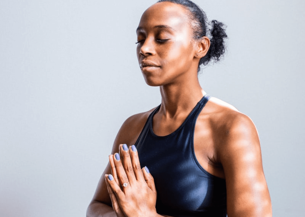 A woman with her hands together in prayer position, with her eyes closed