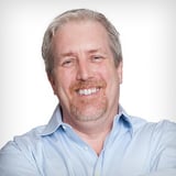 Alexoo pictured from the shoulders up under neon blue and organge lights. They wear a pair of black sunglasses