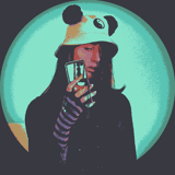 an individual standing to take a mirror selfie, wearing a suit, tight arm warmers, and a white bucket hat with a puffball resembling a panda's ears on each side