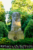 A photograph of a stone sphinx monument surrounded by vegetation