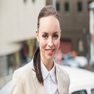 A young woman with brown hair and brown eyes in a flower shop, smiling and holding a rose close to her face