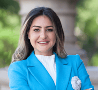 State Representative Mihaela Plesa in a white shirt, turquoise jacket standing in front of the Texas State Capitol