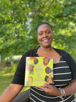 Ms. Nichole outside pictured smiling and holding a copy of her new children’s picture book.