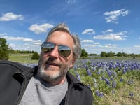 Ed Stevens laying in a field of bluebonnets on a sunny day.