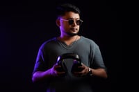 DJ MIJO pictured from the shoulders up under neon blue and organge lights. They wear a pair of black sunglasses