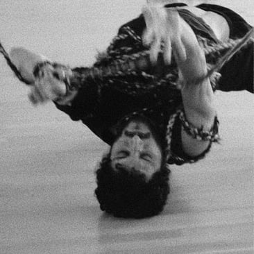 Grainy black and white photo of a dancer captured mid-movement upside down, arms outstretched.