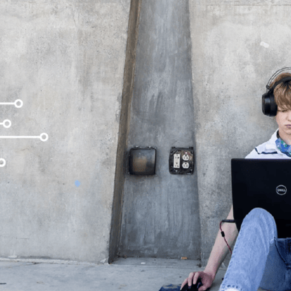 A young person wearing headphones sits on the ground with a Dell laptop, using a mouse beside them. They are positioned against a concrete wall with a white circuit-board graphic along the left side.