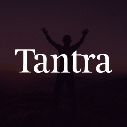 Shirtless man with his arms in the air looking towards a mountainside sunset